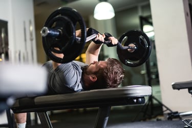A man performing a triceps extension with a weighted barbell on a weight bench at the gym.