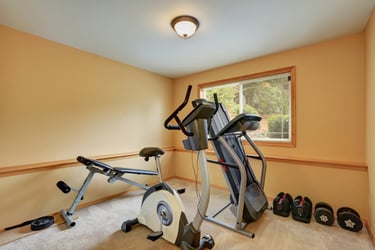 Home gym setup with an exercise bike, treadmill, weights, and a workout bench.