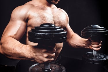 Muscular shirtless man performing a seated dumbbell bicep curl for strength training.