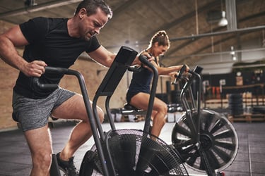 Man and woman performing high-intensity interval training on air bikes at a modern gym.
