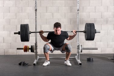 A man performing a heavy barbell back squat in a power rack at a home gym with knee sleeves.
