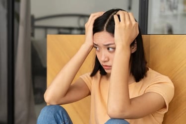 Une femme assise au sol, les mains sur la tête, exprimant une émotion de détresse ou d’angoisse.