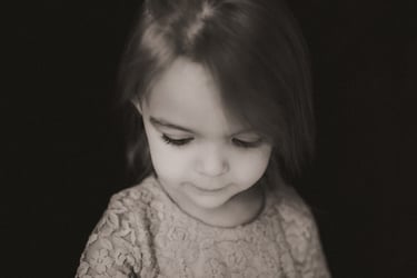 Two-year-old girl looking down thoughtfully against a black backdrop during a personality portrait s