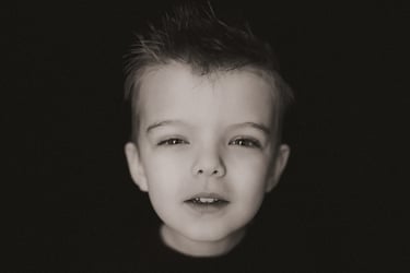 4-year-old boy squints curiously into the camera during a personality portrait session on a black ba