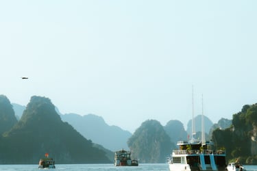 Boats sailing in Ha Long Bay, in Vietnam. In the distance are mountains and a beautiful blue sky.
