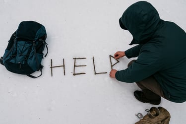 Survivalist writing HELP with sticks in snow near backpack for emergency rescue signal