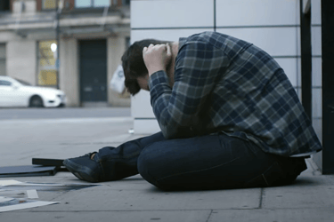 a man sitting on the sidewalk in front of a building