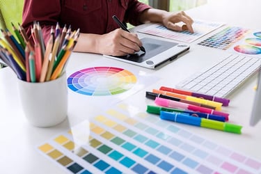 alt="Graphic design computer work station with assorted color samples pencils and pens"