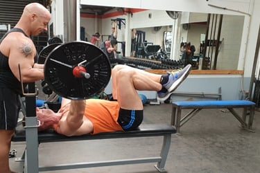 A top Gym coach carefully spotting a man doing a bench press in a gym