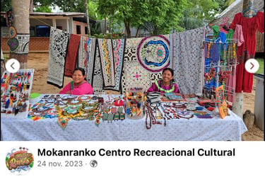 Two indigenous women selling handmade beaded jewelry and embroidered Shipibo textiles at an outdoor market.