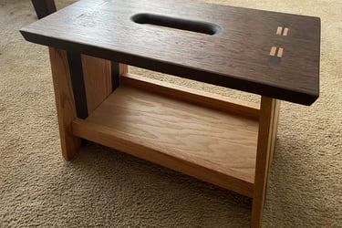 Handcrafted walnut and oak wood step stool with carry handle and decorative joinery on a carpeted floor.
