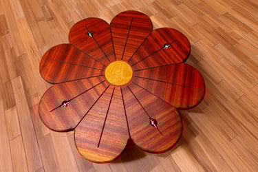 Handcrafted wooden tensegrity table shaped like a flower with mahogany petals on a hardwood floor.
