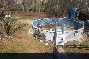 Above-ground swimming pool in a residential backyard with a wooden fence and seasonal landscaping.