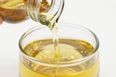 Close-up of golden refined sunflower oil pouring into a clear glass container, bright natural light, crisp reflections.
