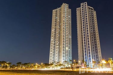 Two modern luxury high-rise residential towers illuminated against a dark night sky in a city.