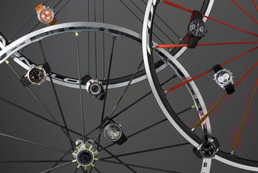 selection of mens watches attached to the spokes of bicycle wheels on a grey background