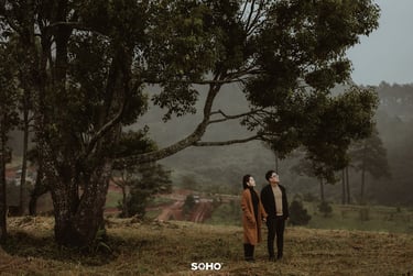 a couple standing in a field with trees in the background
