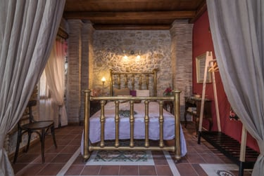 Open space bedroom with rustic bed and vintage elements, wisely separated from living area by curtains in Villa Galanoussa