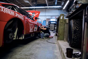 A mechanic performs professional maintenance on a red Ferrari race car in an automotive repair shop.