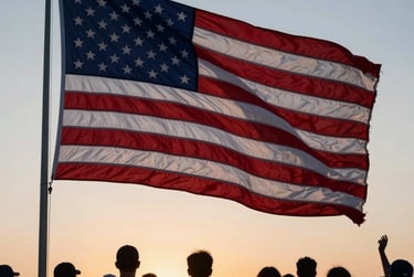 Crowd of people silhouetted against a sunset watching a large American flag waving on a flagpole.