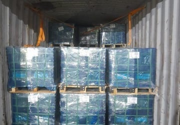 Stacked pallets of shrink-wrapped cargo loaded inside a metal shipping container for transport.