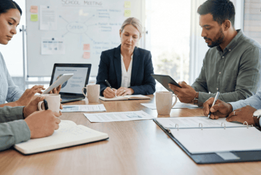 Diverse business professionals collaborating in a corporate office meeting with tablets and notebooks.