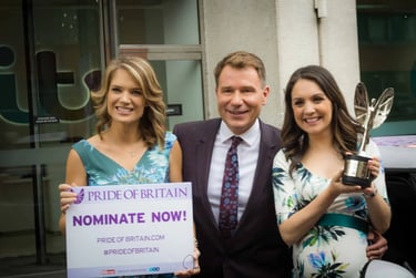 ITV presenters holding a Pride of Britain nomination sign and award trophy outside a studio.