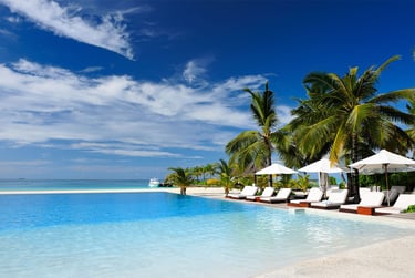 Beach front hotel swimming pool with sunbeds and parasols with palm trees and blue sky