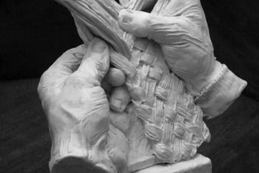 A detailed clay sculpture of two hands skillfully weaving a basket with long fibers on a square base.
