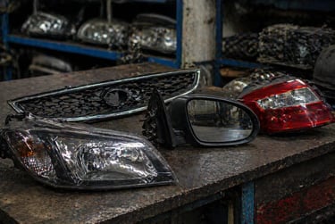 Peças de carro em bancada de oficina com farol e retrovisor de veículo popular no Brasil