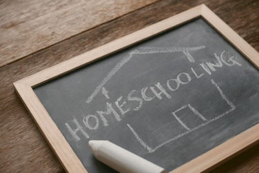 Homeschooling word and house outline drawn in chalk on a black chalkboard on a wooden table.