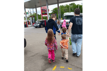 A family with several small children walking through a gas station parking lot together.