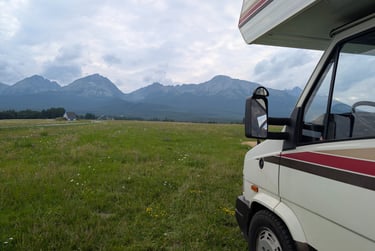 Camper parked on a grassy field with the High Tatras mountains in the background under a cloudy sky