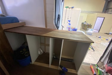 Custom camper van kitchen renovation featuring a wooden butcher block countertop and white cabinets.