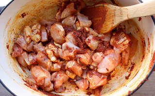 raw chicken cooking in a large pot with the red curry paste
