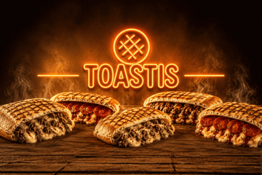 Delicious toasted panini sandwiches with melted cheese and beef under a glowing Toastis neon sign.