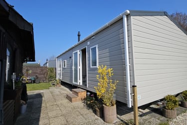 Modern grey mobile home with white trim and a stone patio under a clear blue sky.