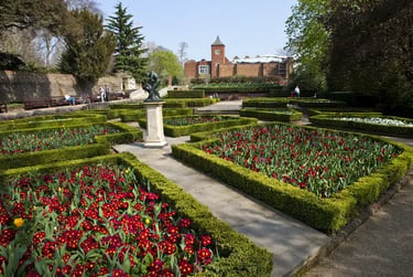 Formal English garden in Holland Park, red primrose flower beds, and a brick manor house in