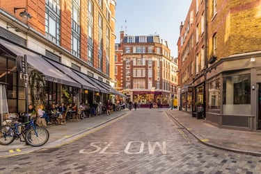 People dining at an outdoor sidewalk cafe on a cobblestone London street with brick buildings.