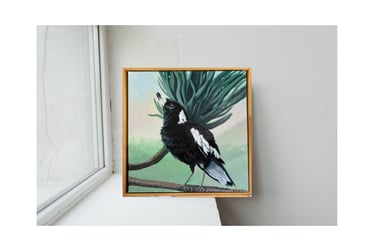 painting of an Australian magpie perched on a branch, framed in wood on a white windowsill.