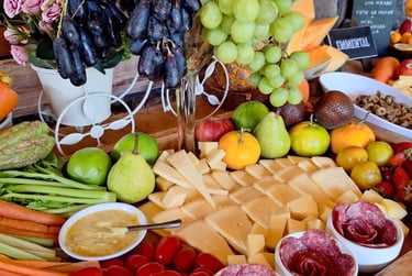 Gourmet charcuterie board with sliced cheese, grapes, strawberries, tomatoes, and salami roses on a wooden tray.