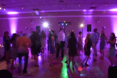 Wedding guests dancing on a wooden dance floor with purple uplighting and disco stage lights.