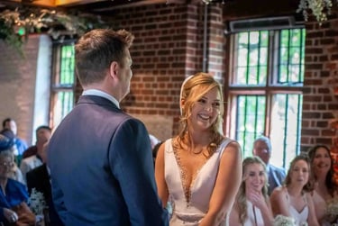 Smiling bride in a white wedding dress exchanging vows with her groom during an indoor ceremony.