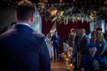 Bride and groom walking down the aisle at an indoor wedding ceremony with floral decor and candles.