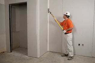 Professional contractor using a drywall corner tool to finish seams in a new interior construction.