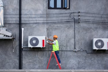 Professional HVAC technician in safety gear repairing an outdoor air conditioning unit on a ladder.