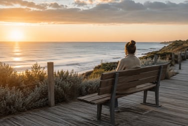 Woman sitting alone on a wooden bench overlooking the ocean at sunrise.  