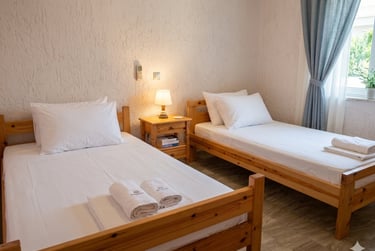 Two single wooden beds with white linens and rolled towels in a bright guest bedroom.