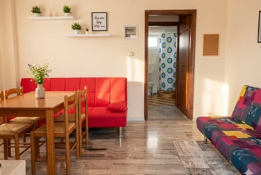 Modern living room with a red sofa, wooden dining table, and marble floor leading to a bathroom.