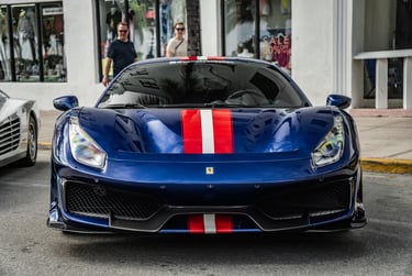 Front view of a blue Ferrari 488 Pista with red and white racing stripes parked on a city street.